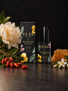 ELAA Bee Beauty bottle and carton with ivory peony, goji berries, honeycomb and white blossoms on dark stone