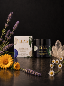 ELAA Morning Dew balm and carton with flowers and crystals on a flat dark surface